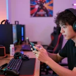 Exciting gaming atmosphere with young adult playing MOD APK games on smartphone, vibrant colors, and accessories.